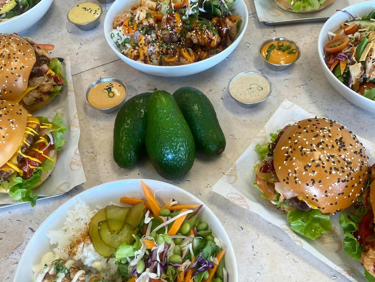 Tablescape of fresh salads, burgers, avocadoes and sauces