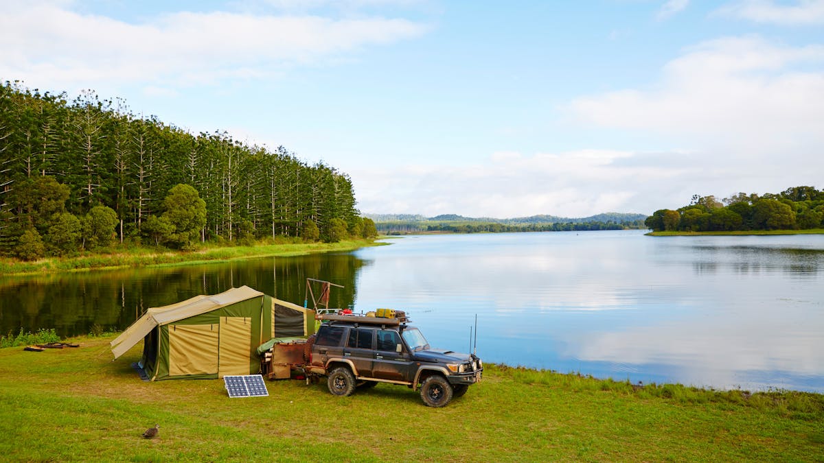 Tent and car are set on the lakes shores with pine forest in background.