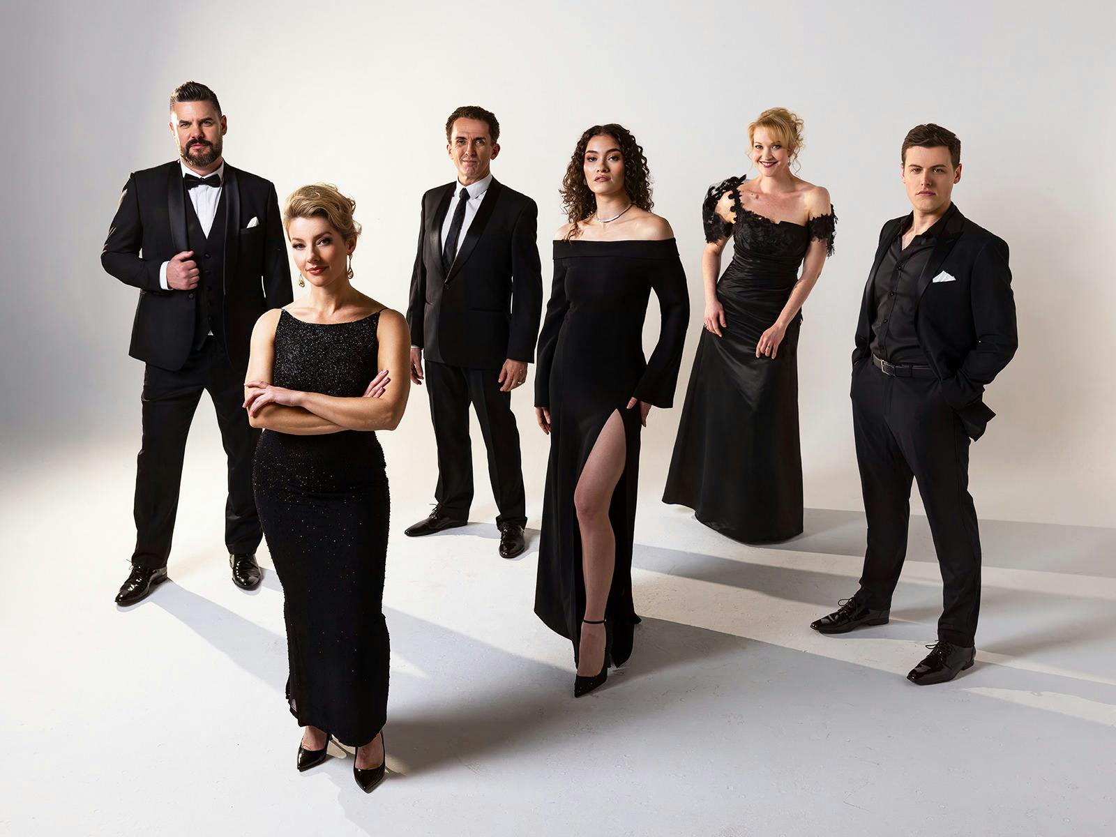 Cast of Gilbert and Sullivan in black formal wear, standing in a group.