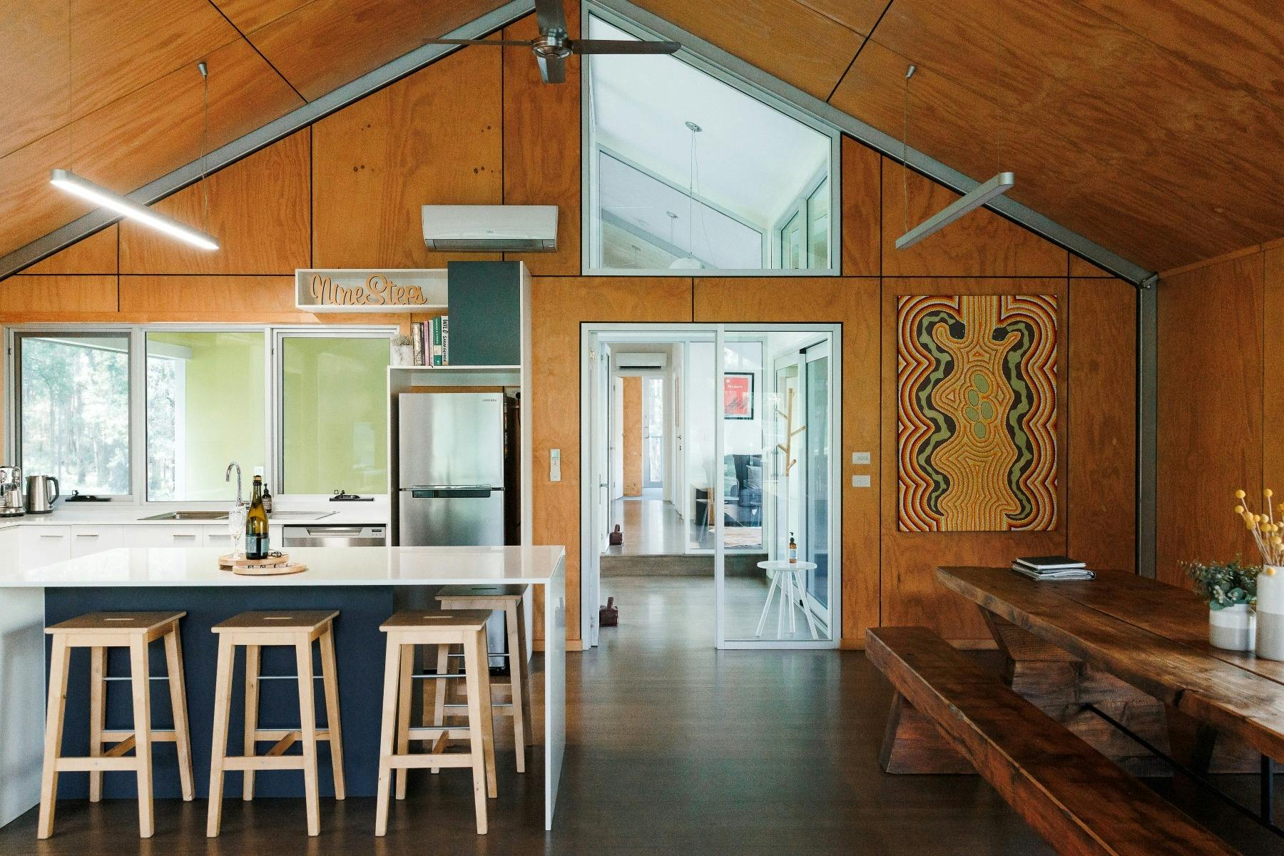 Large white and navy blue kitchen, wooden dining table, ply walls, large Indigenous painting
