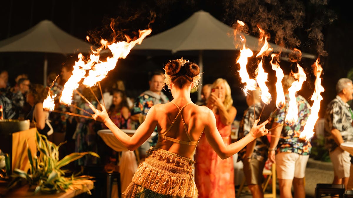 Image of a female fire performer holding a fire staff in each hand with guests watching