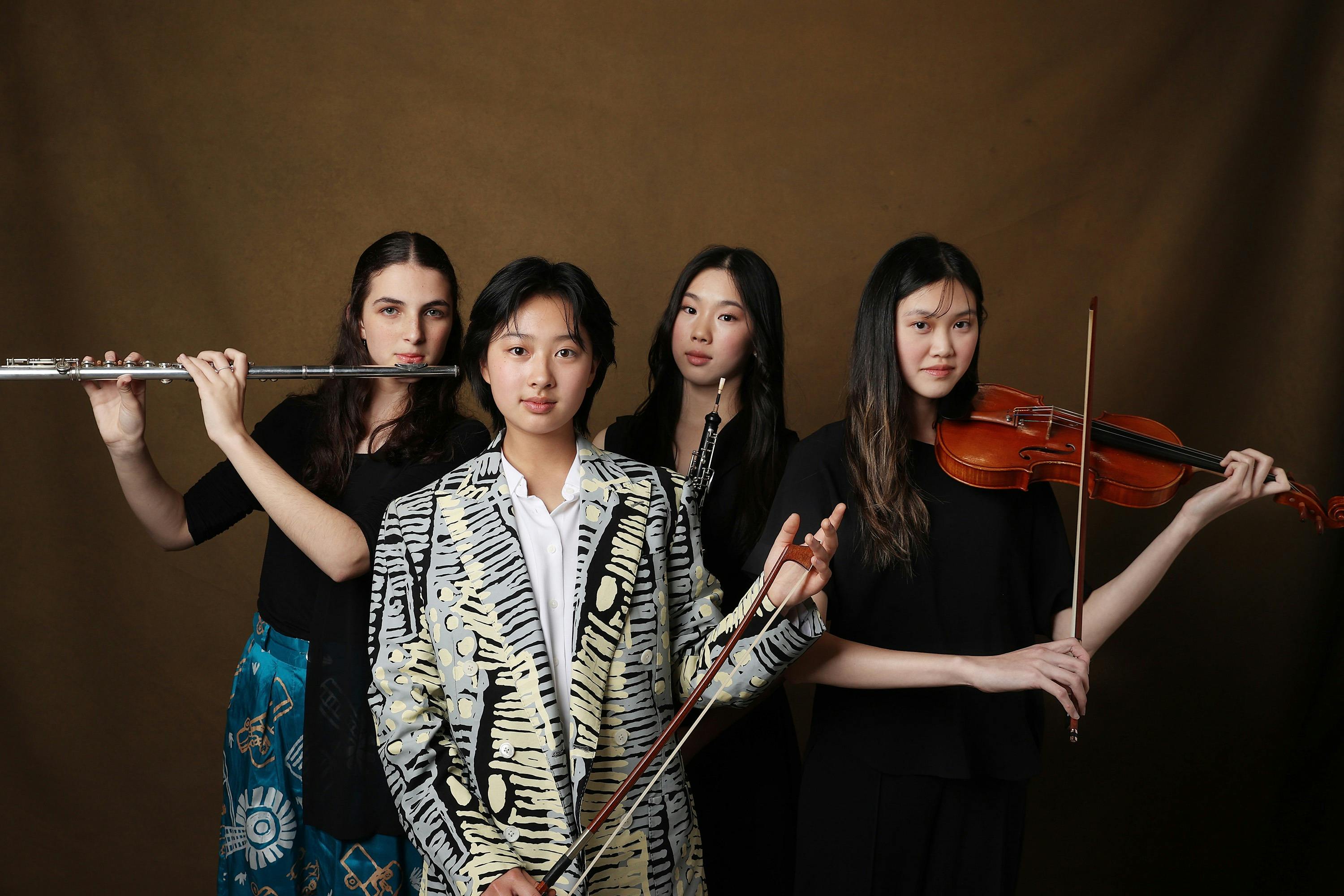 Four young people looking into the camera, holding a flute, bass bow, oboe and violin.