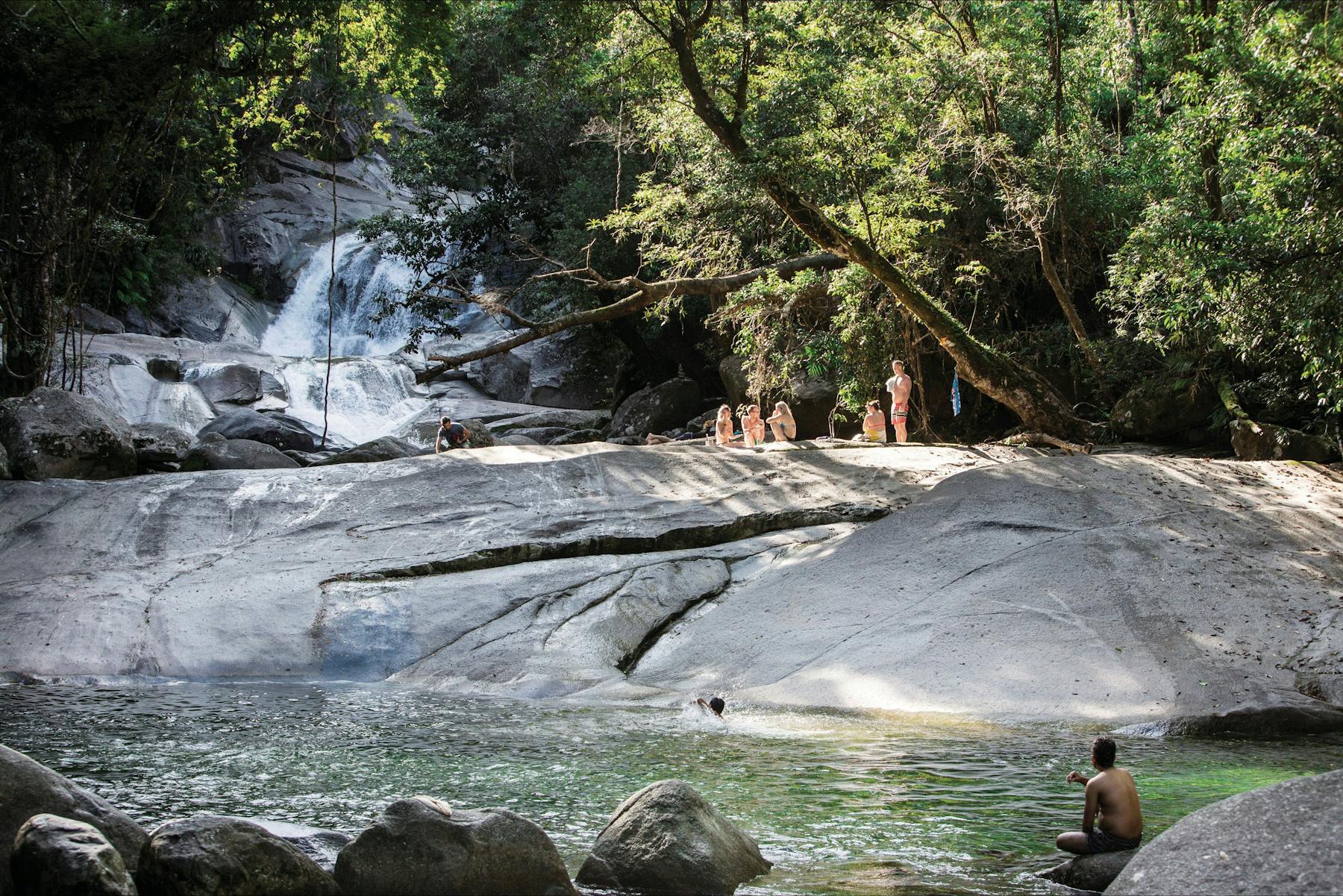 People on rock above bottom pool with waterfall in background.