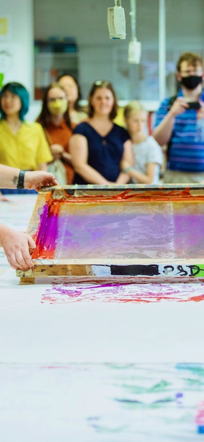 Two women lift a large colourful screen after printing