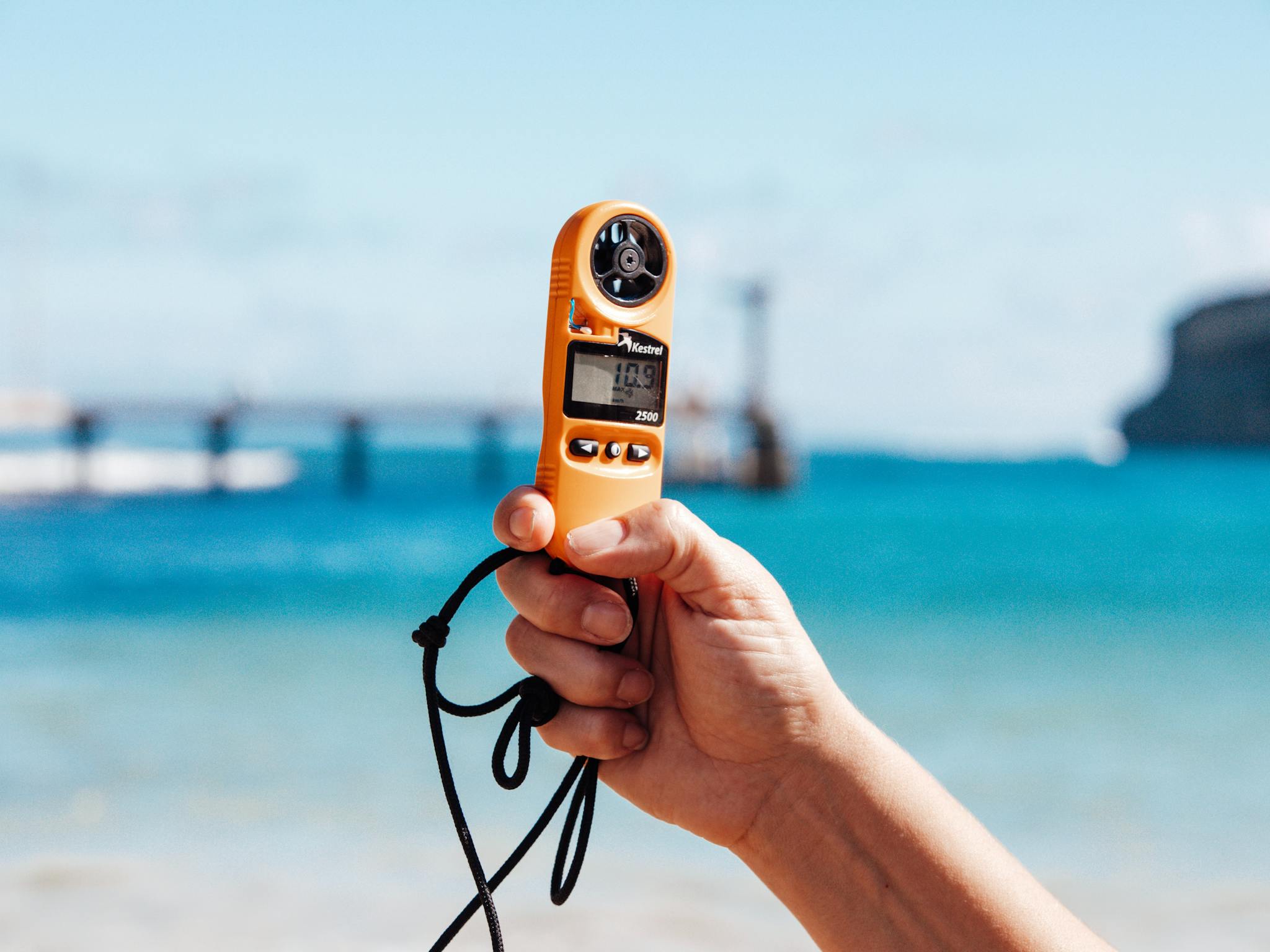 Hand holding an anemometer with the Port Campbell Jetty in the background