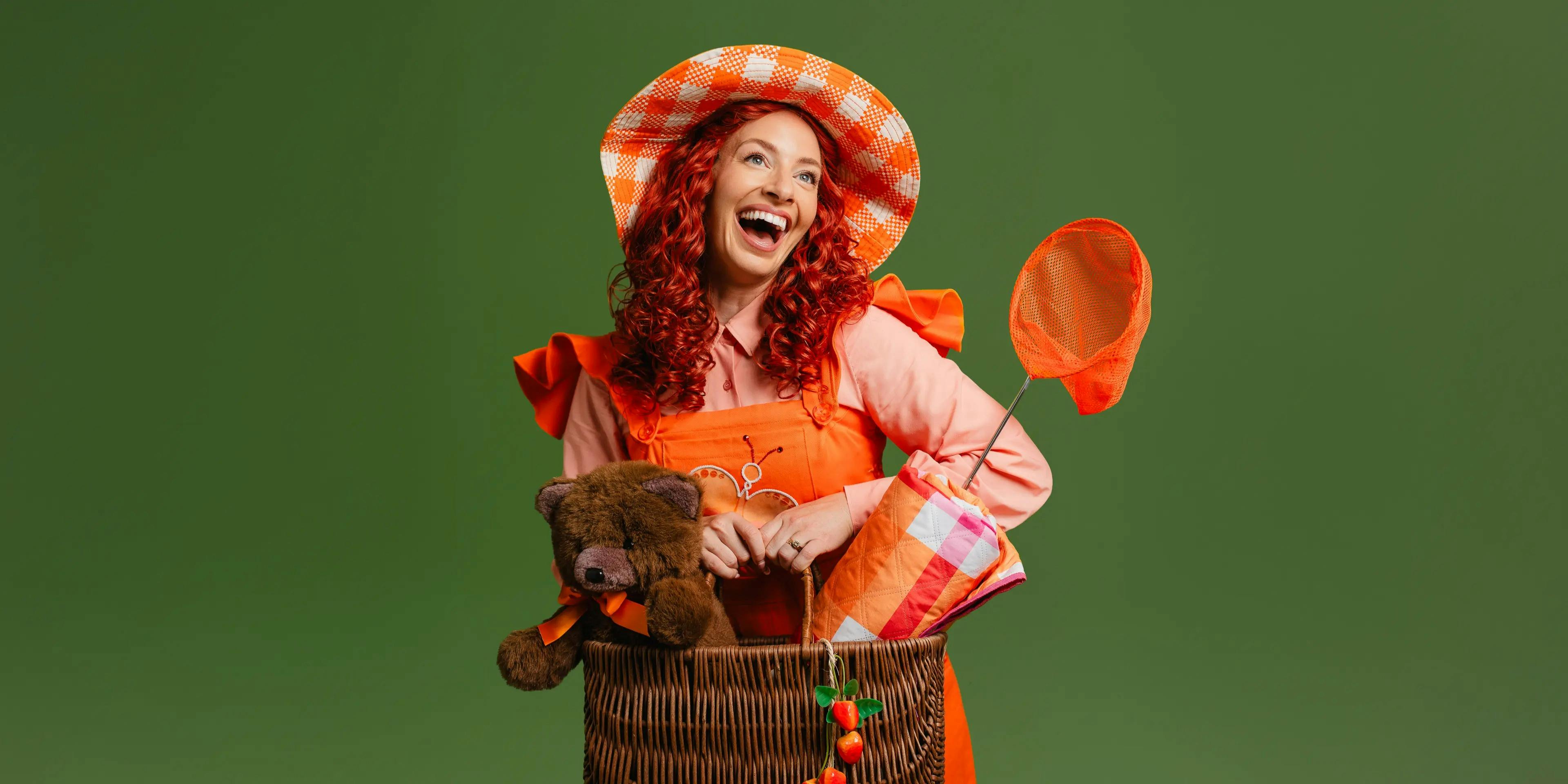 A lady dressed in Orange with bright orange hair and a bag with a teddy bear and net