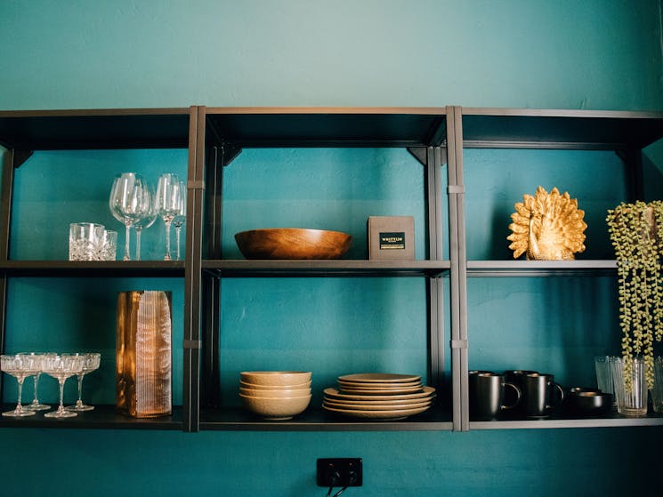 Black shelves with black crockery, wine glasses set against a bright teal wall.