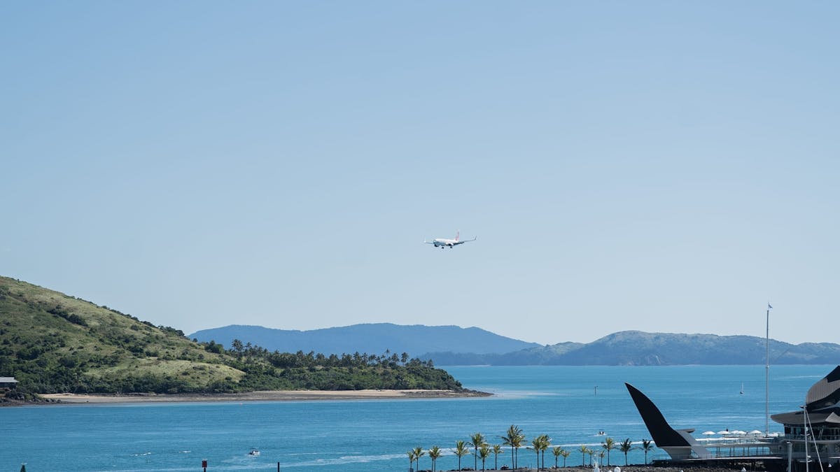 A plane arriving in the distant to the island airport beside the blue ocean