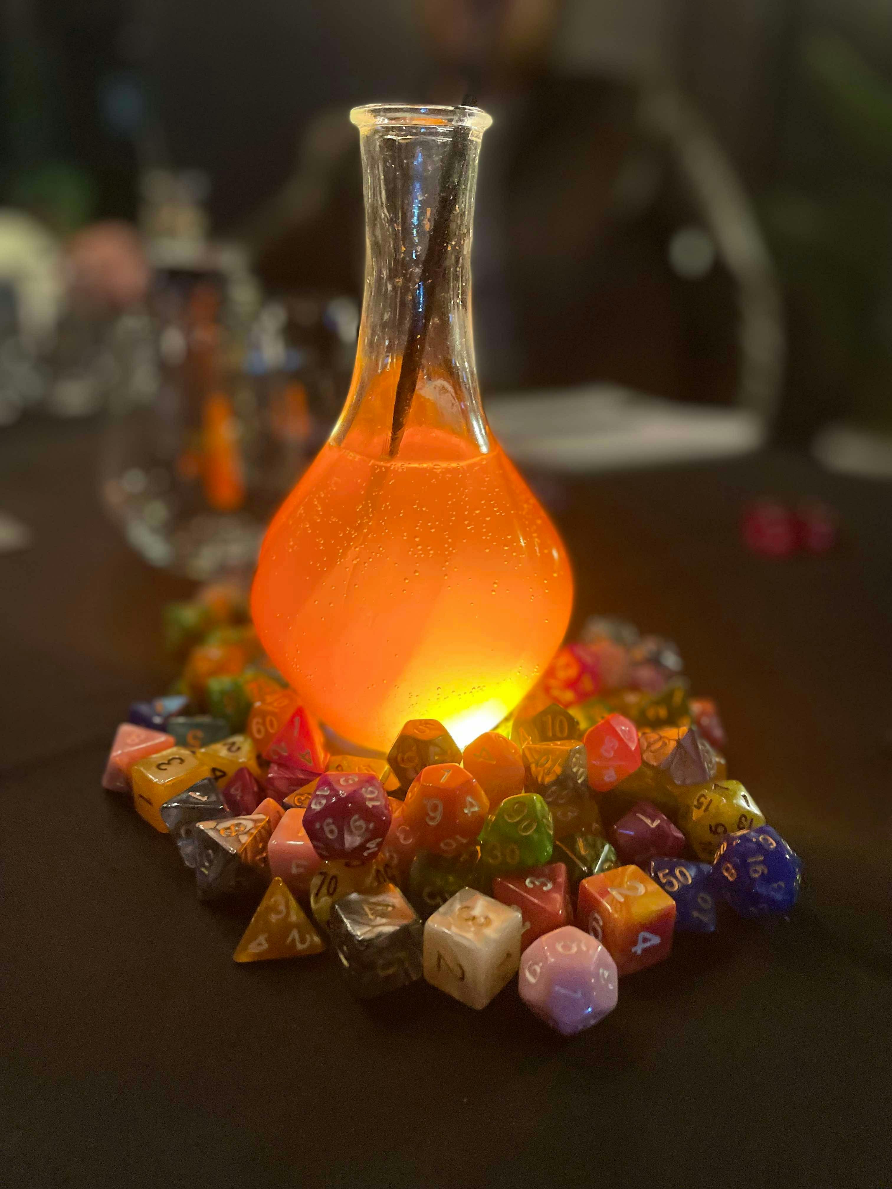 gold potion cocktail surrounded by a mound of colourful dice.