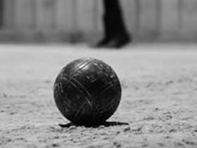 A black and white photo of a petanque ball sitting on grass with a person standing away from it.