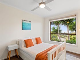 Bright bedroom with king bed, white linens, orange accents, ceiling fan, and bay views.
