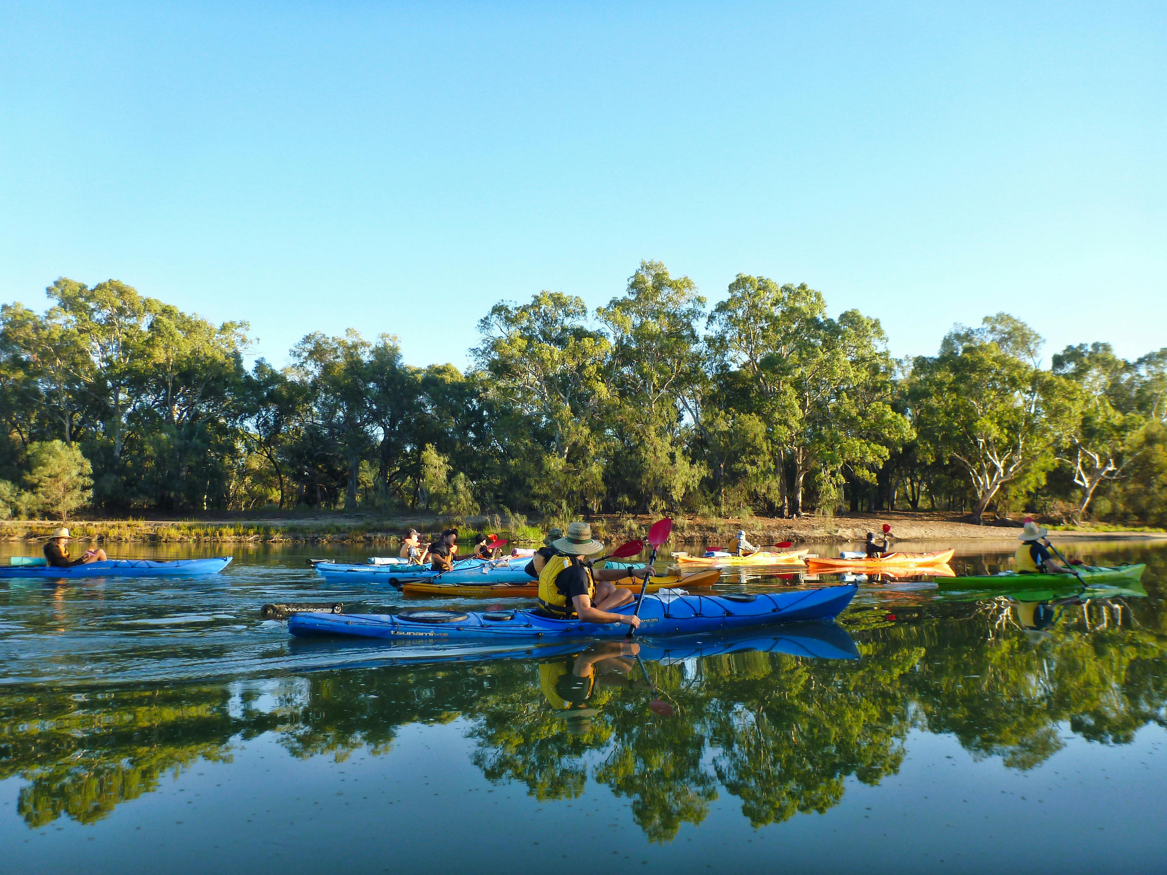 In late afternoon light, on glassy waters, a school group of kayakers paddles upriver.