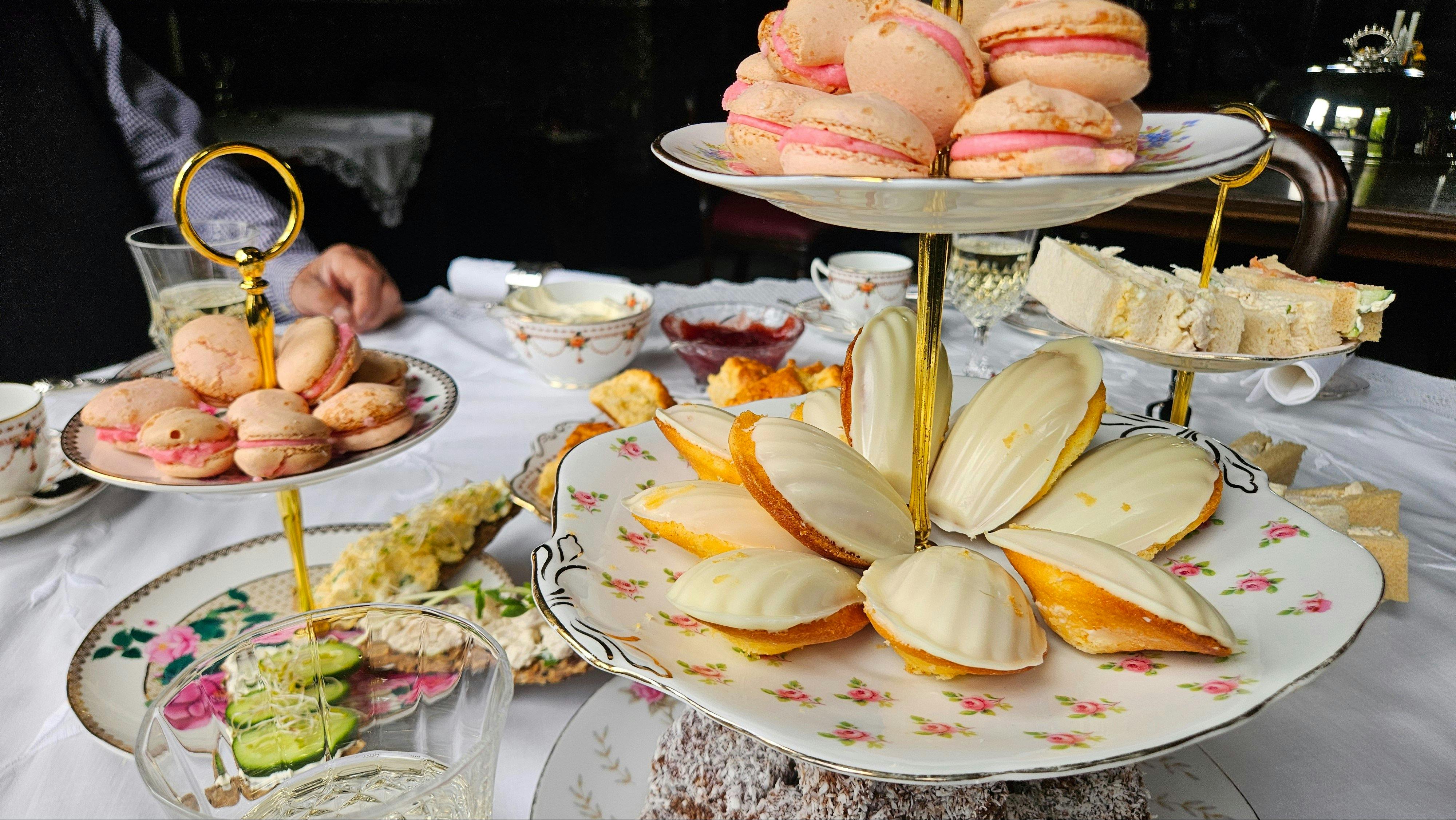 Tea poured beside macarons and madeleines on a tiered stand