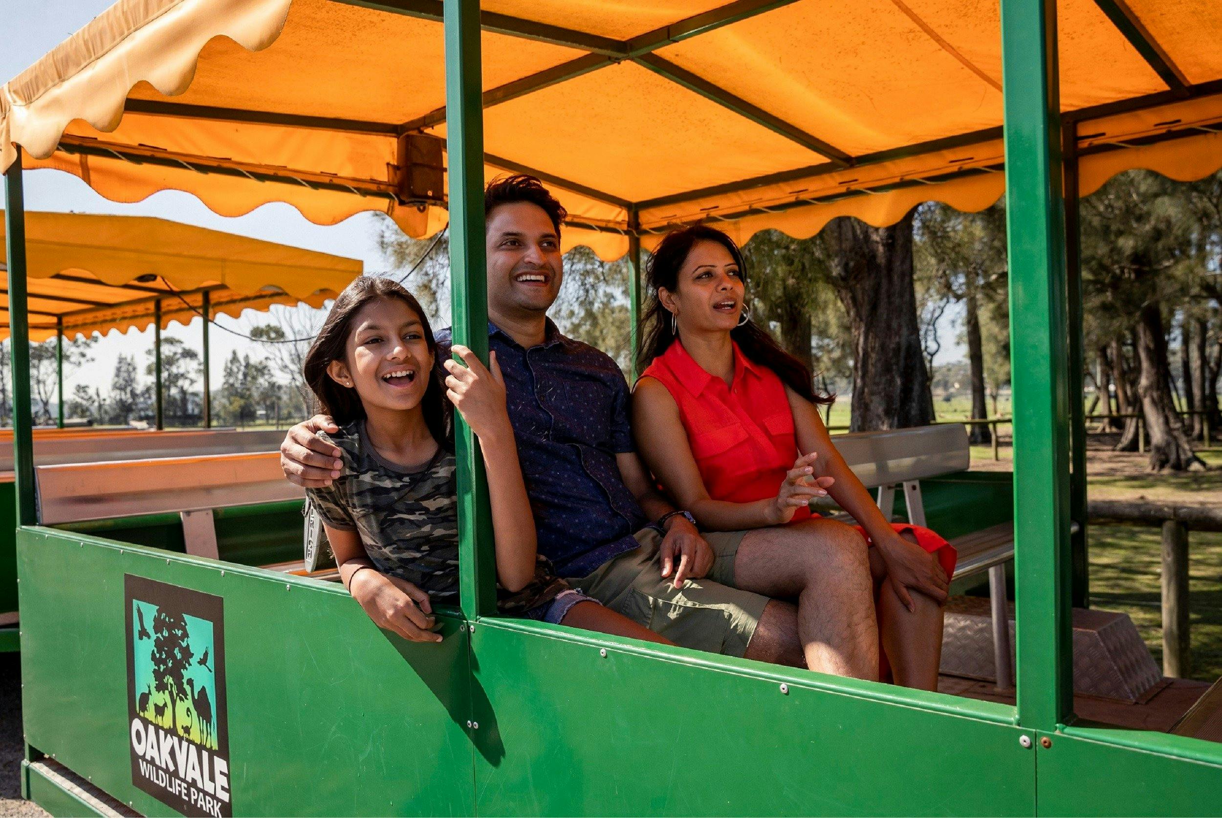 A mum, dad and child smiling and enjoying a tractor ride around the park