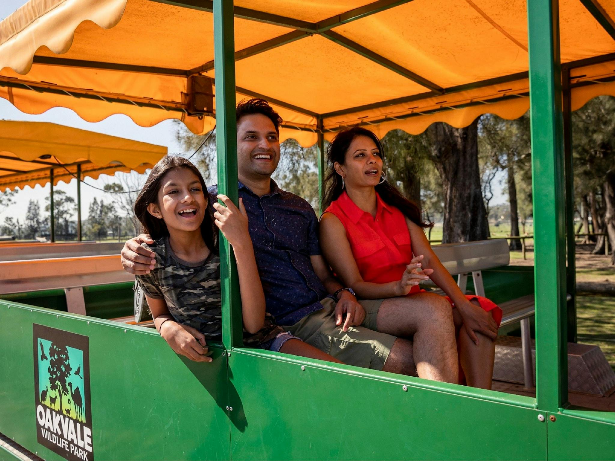 A mum, dad and child smiling and enjoying a tractor ride around the park