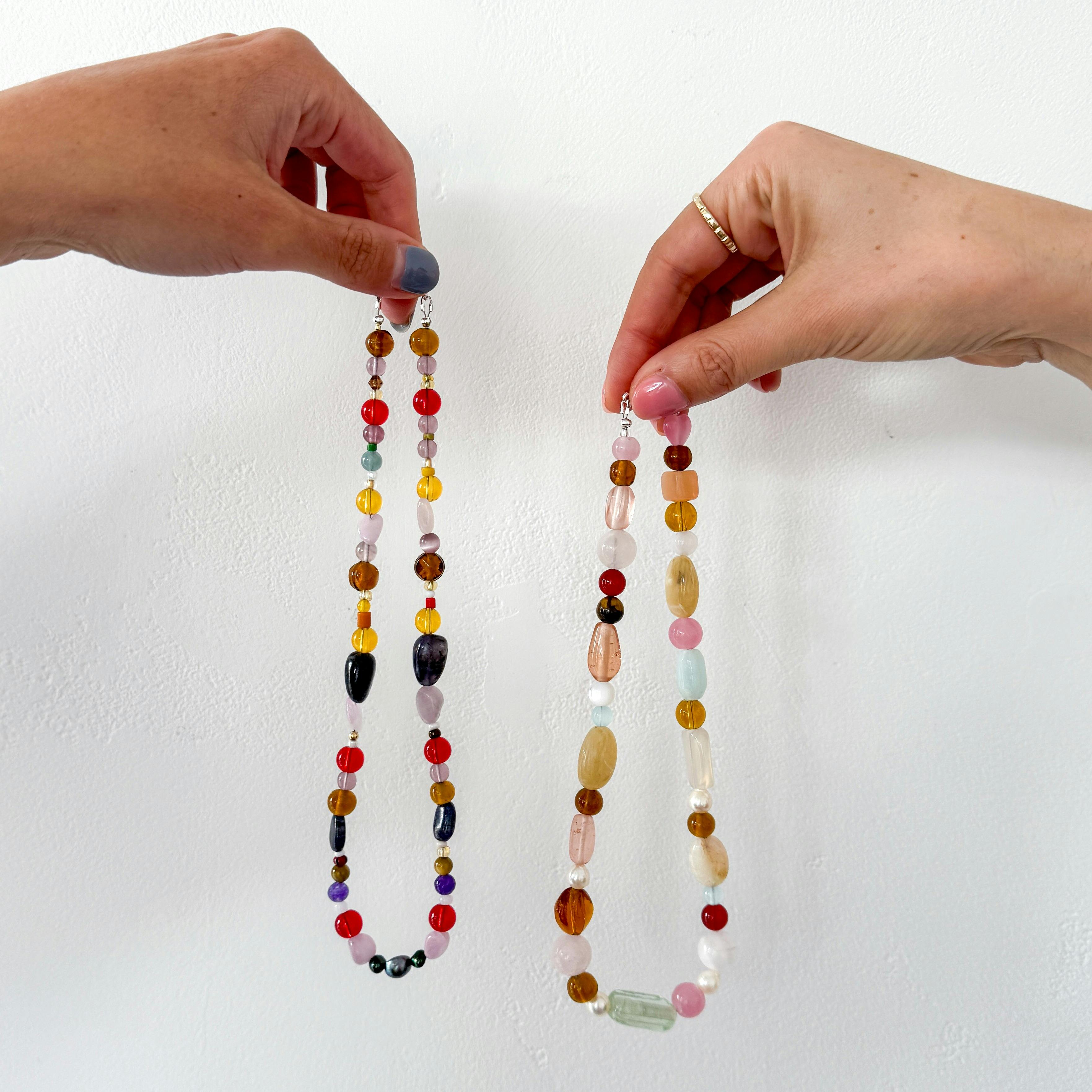 Two hands holding colourful beaded necklaces