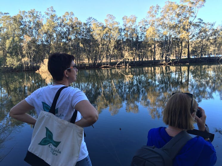 Guide and visitor at the rivers edge, with reflections of the trees that line the river banks.