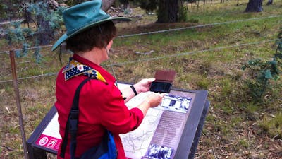 Woman in red shirt holding smart phone over an information panel in bush