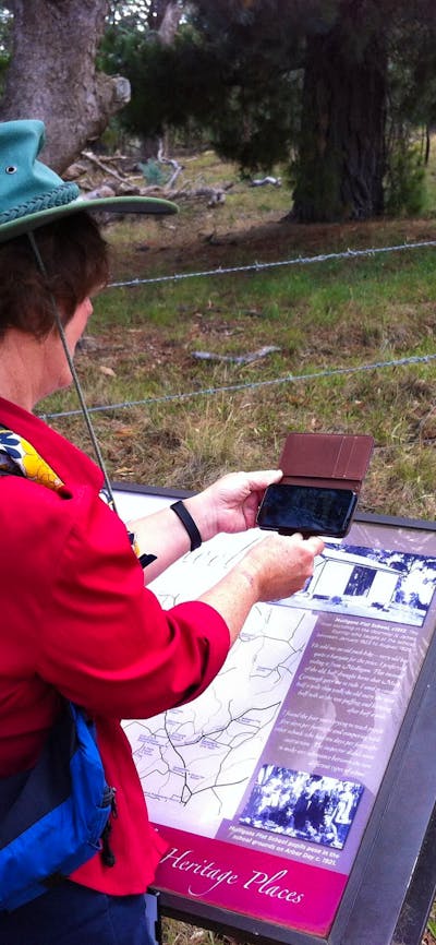 Woman in red shirt holding smart phone over an information panel in bush