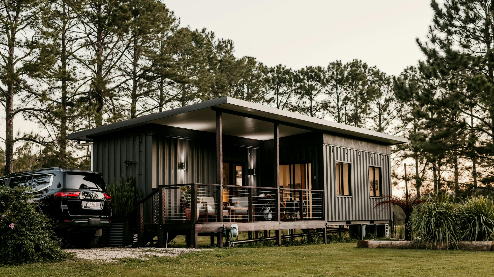 Eco cabin built from shipping containers, set among pine trees at sunset in Nimbin, Australia.