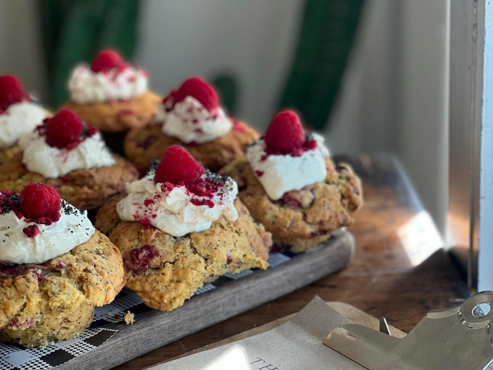 A tray of muffins topped with coconut cream and raspberries
