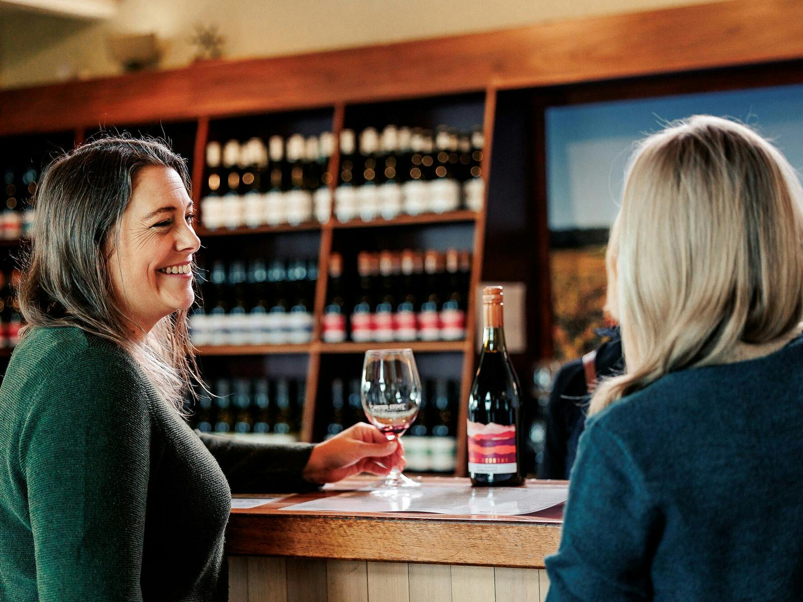 Two women at a tasting bar with a glass and bottle of wine