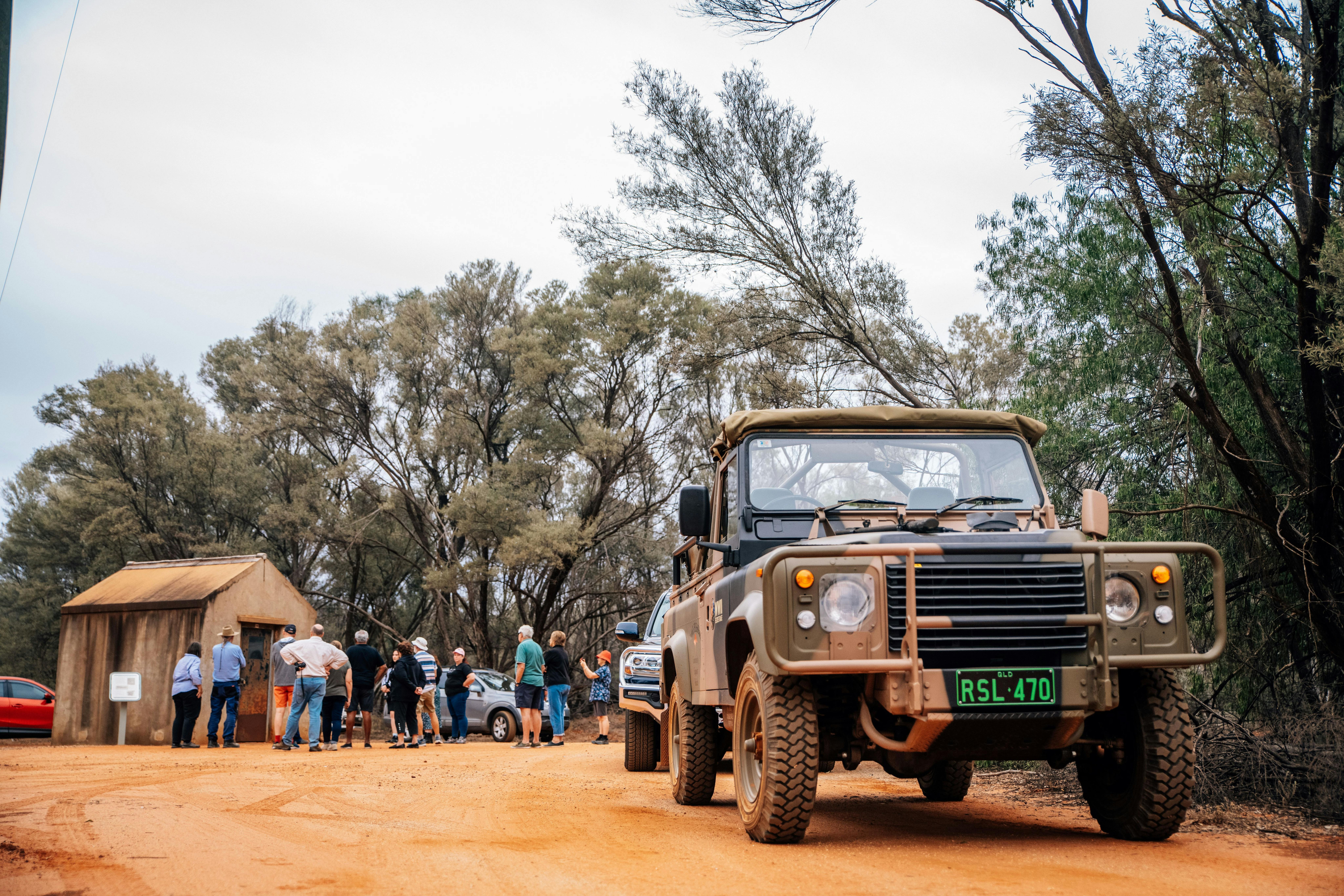 A group of tourists listening to a guide in the background with a military vehicle in the foreground