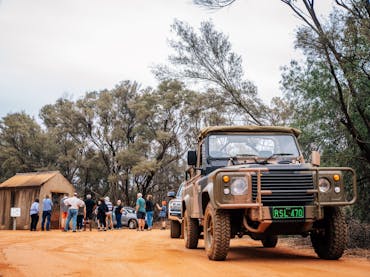A group of tourists listening to a guide in the background with a military vehicle in the foreground A group of tourists listening to a guide in the background with a military vehicle in the foreground