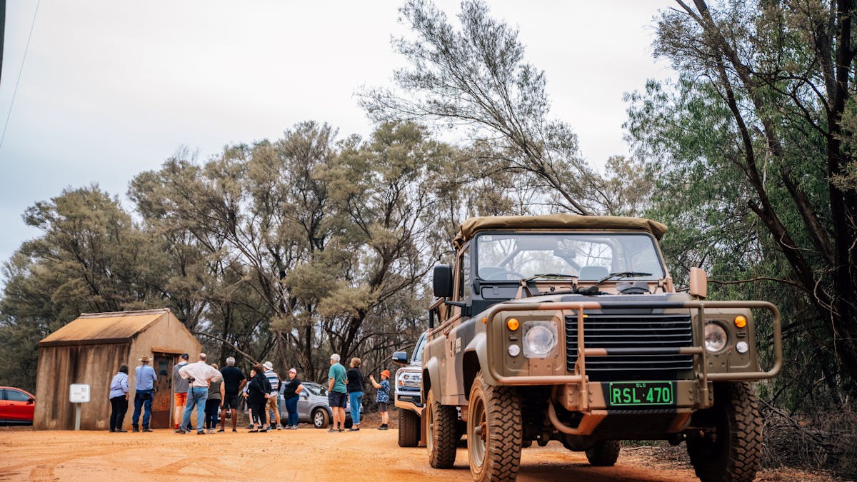 A group of tourists listening to a guide in the background with a military vehicle in the foreground