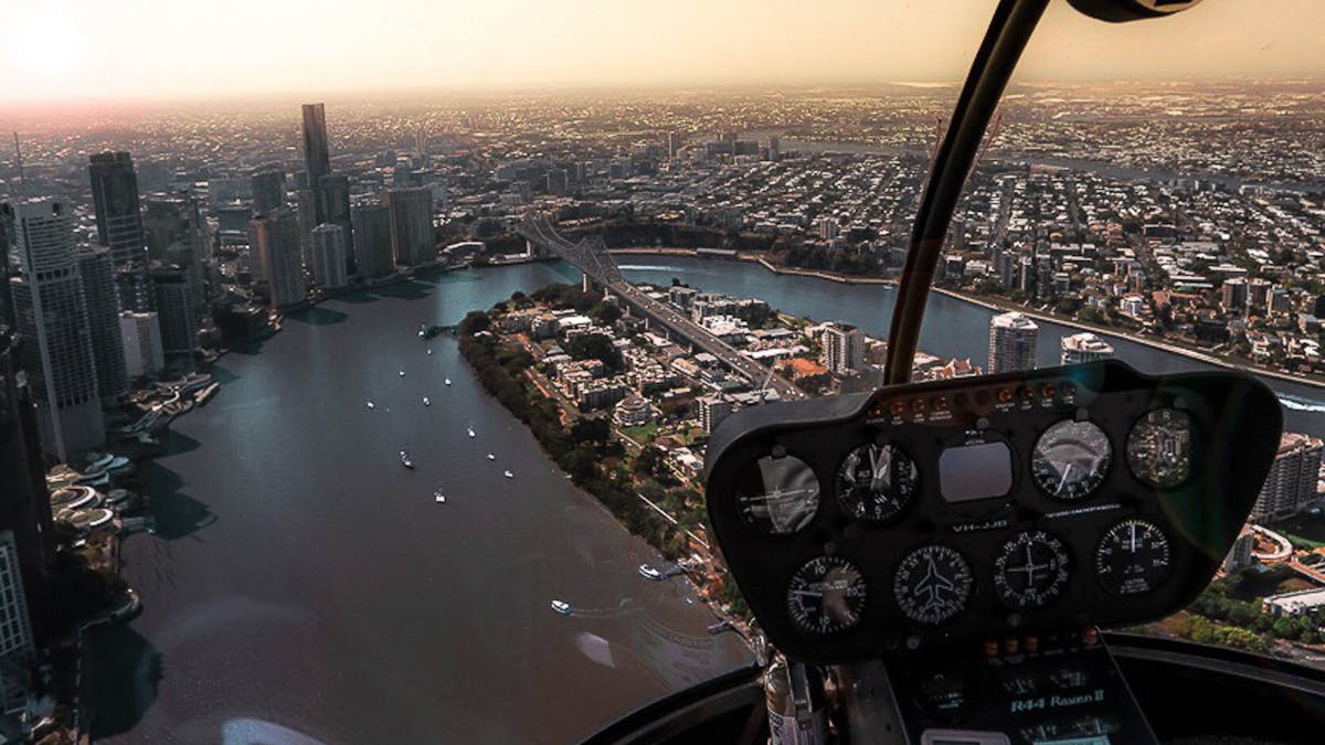 Helicopter cockpit view over Brisbane River and skyline at sunset.