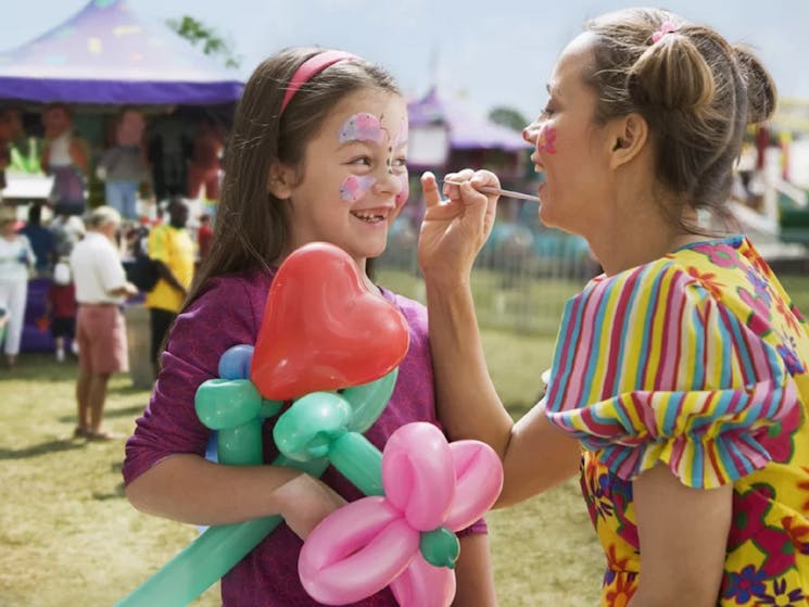 Ypung woman in rainbow clothing facepainting a young girl at a festival