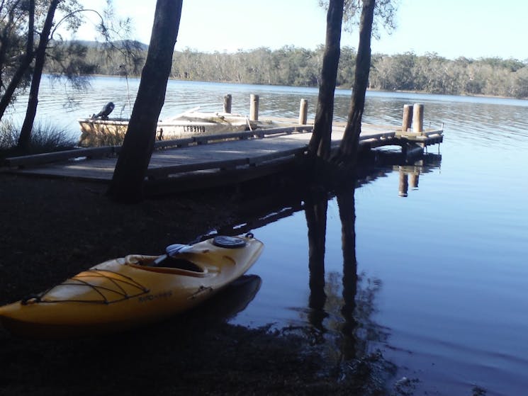 A kayak sitting on the bank od the lake with a jetty in the background  Myall Lakes Kayak Adventure