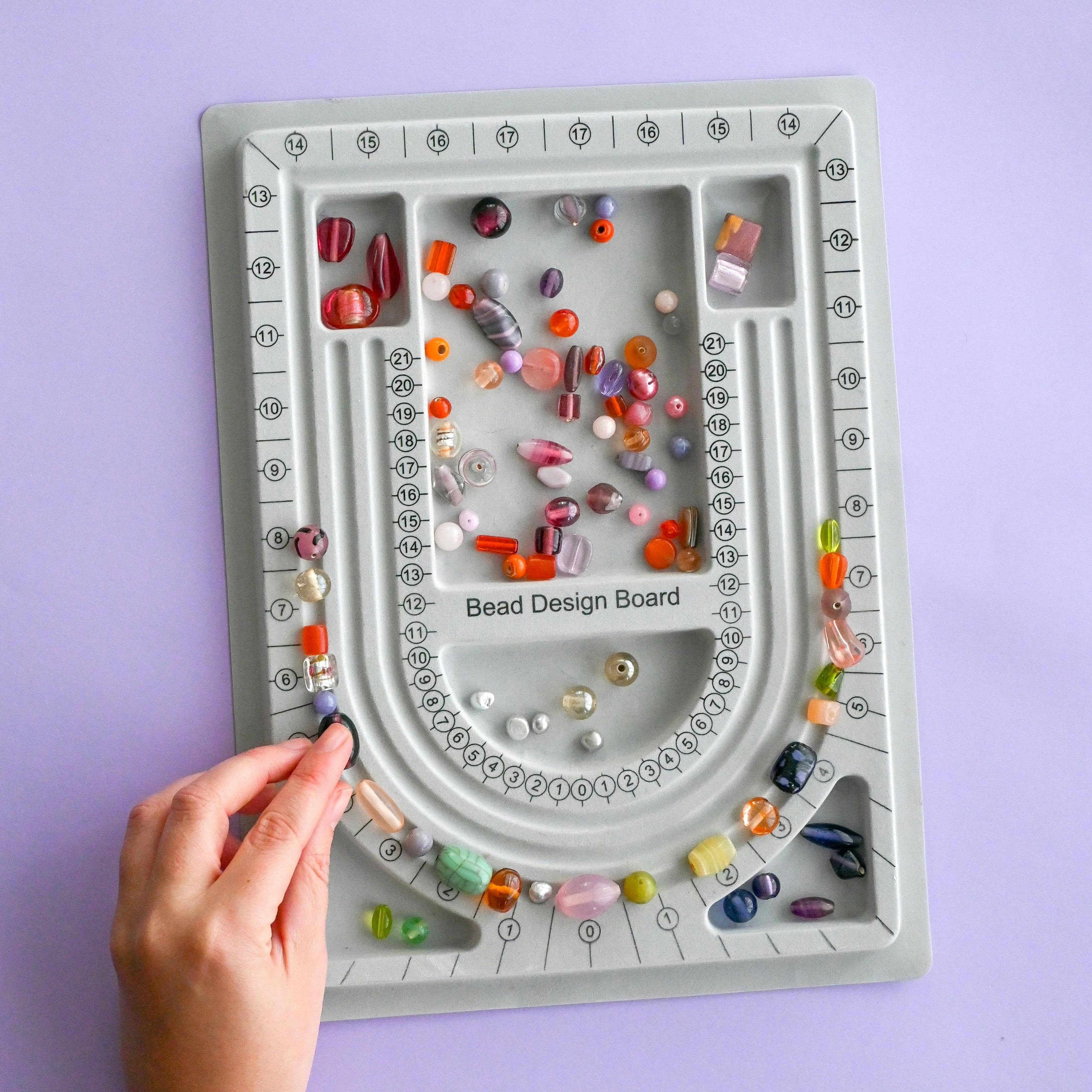 A grey bead design board on a table with hands reaching in moving beads around
