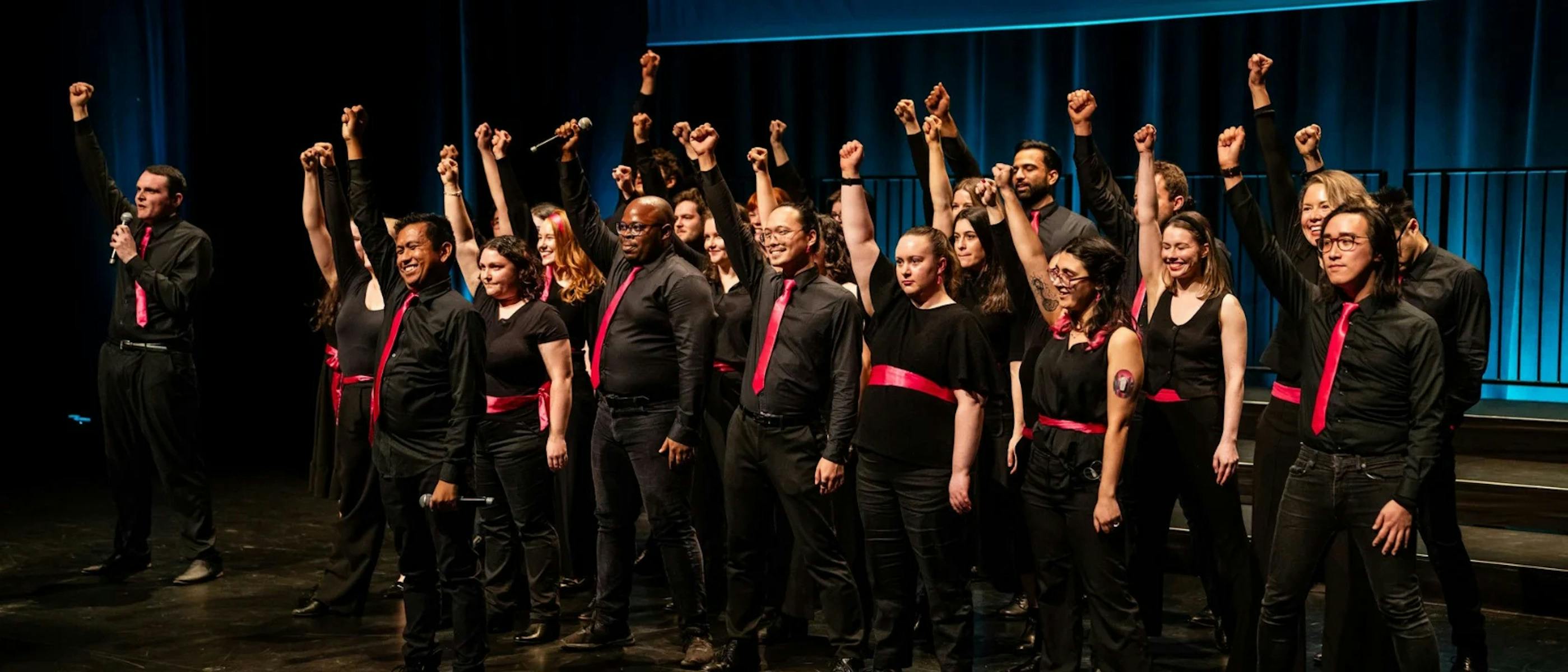 A group of singers wearing black with red, one hand raised