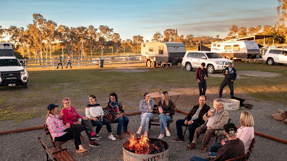 People sitting around a fire pit at sunset in Mackay Region with Campervans