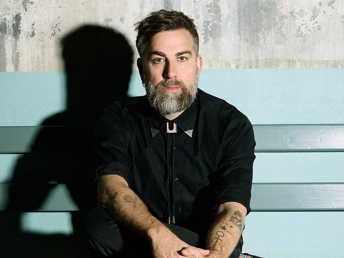 One male with a beard and wearing a black shirt, sitting on a bench.