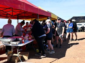 people lining up to get their bbq lunch at the front or a marquee
