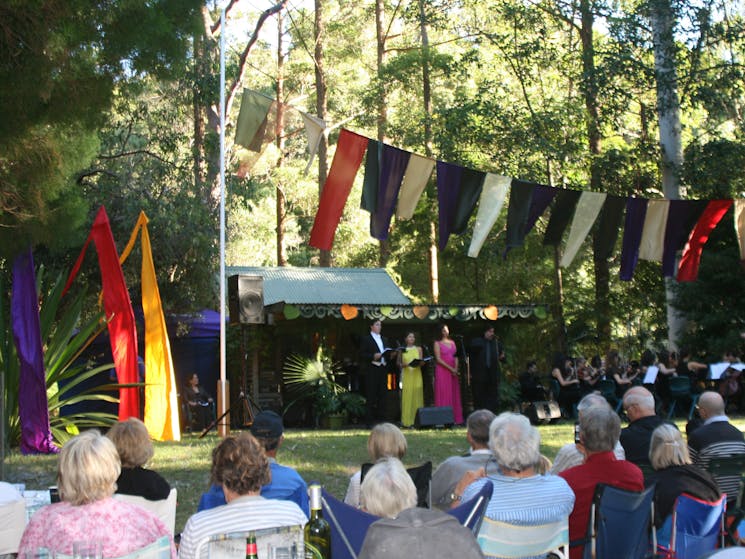 A musical event at the Arboretum. Colourful flags flying above the audience.