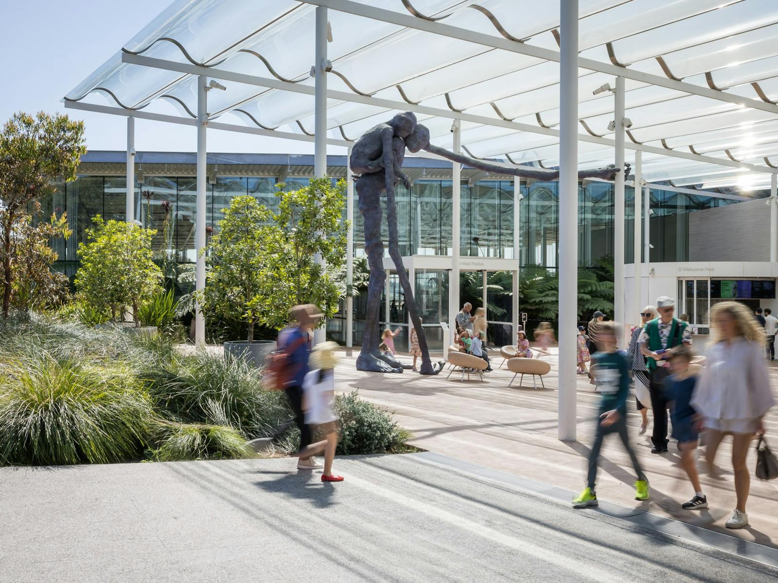 後ろに青い彫刻があるギャラリーのガラス張りのウェルカムプラザに到着したり、出発したりする人々