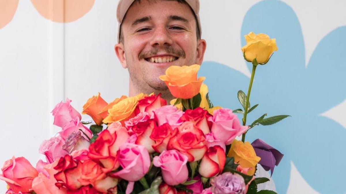 A smiling man holding a large, colourful bouquet of roses, representing a heartfelt act of kindness