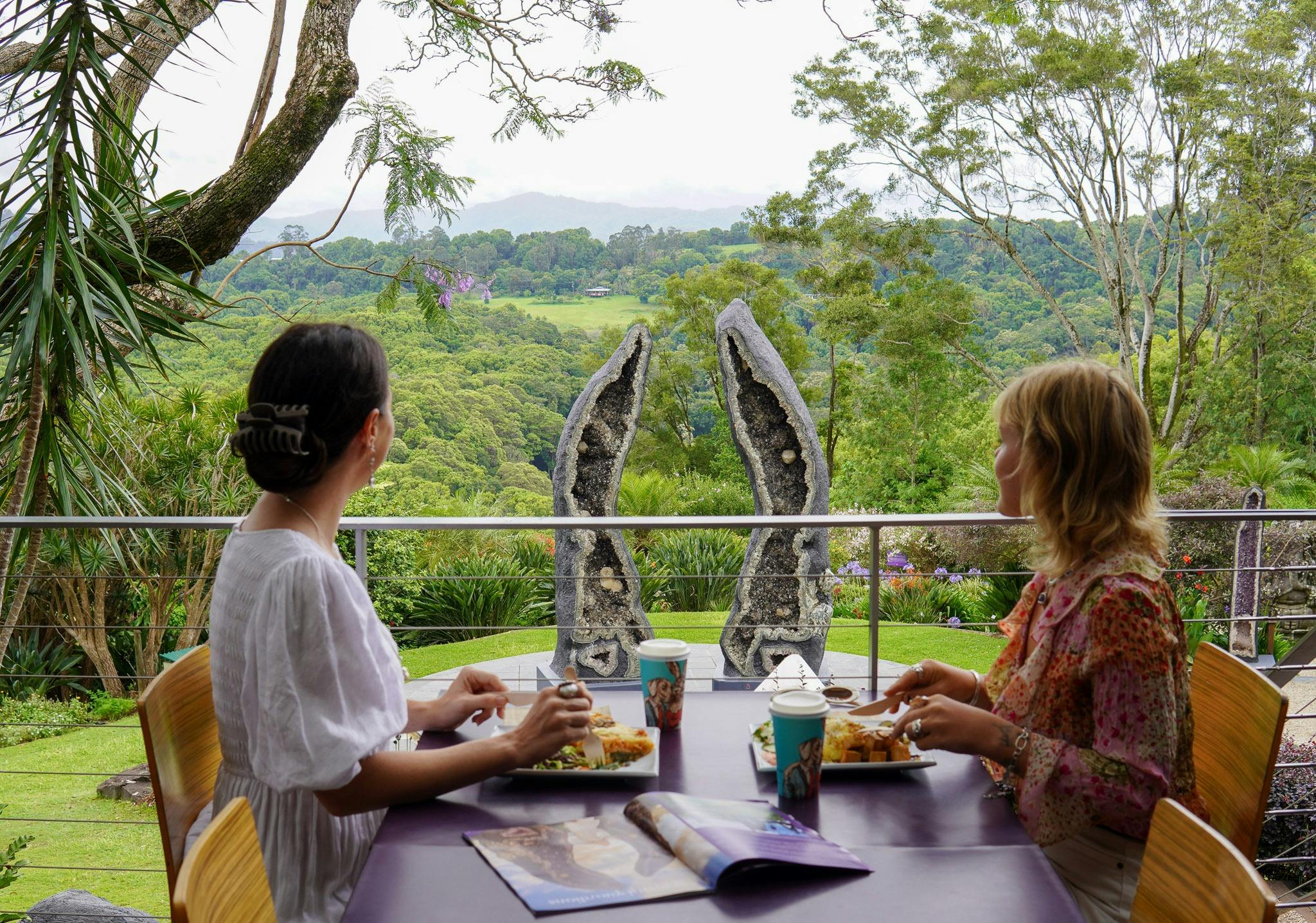 Two friends having lunch at the Lotus Cafe, overlooking the Crystal Guardians geode