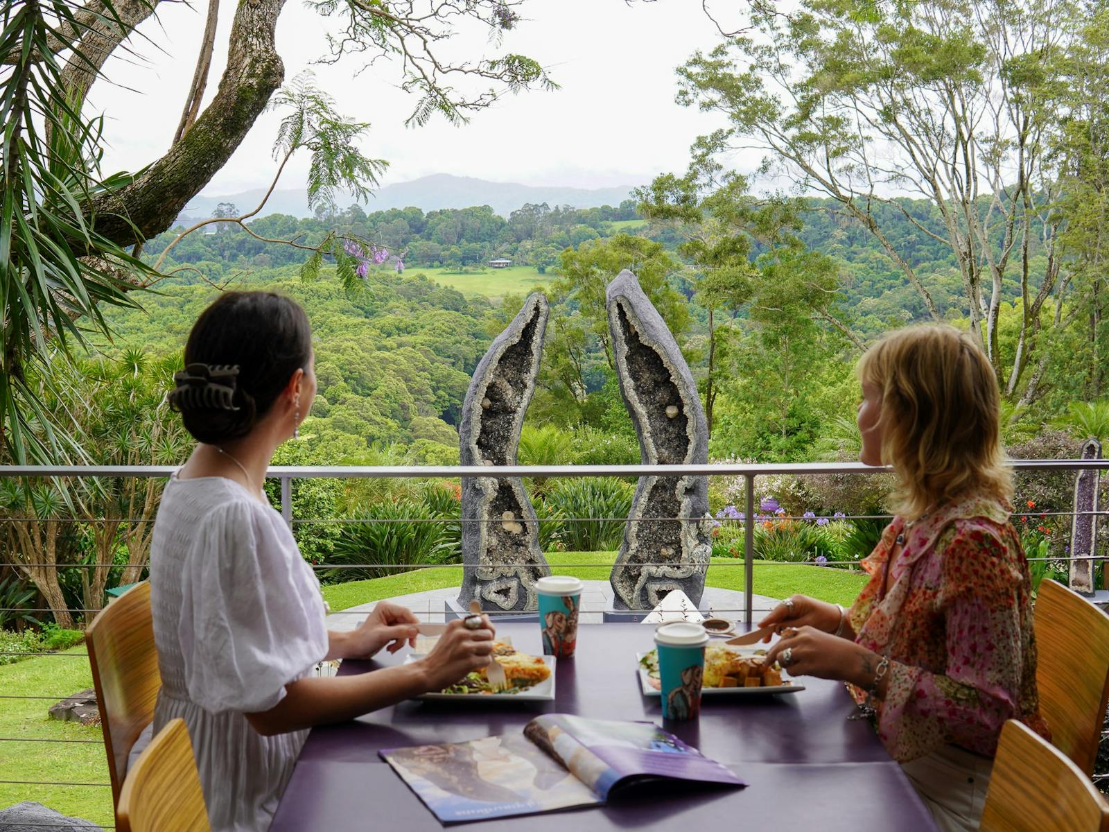 Two friends having lunch at the Lotus Cafe, overlooking the Crystal Guardians geode