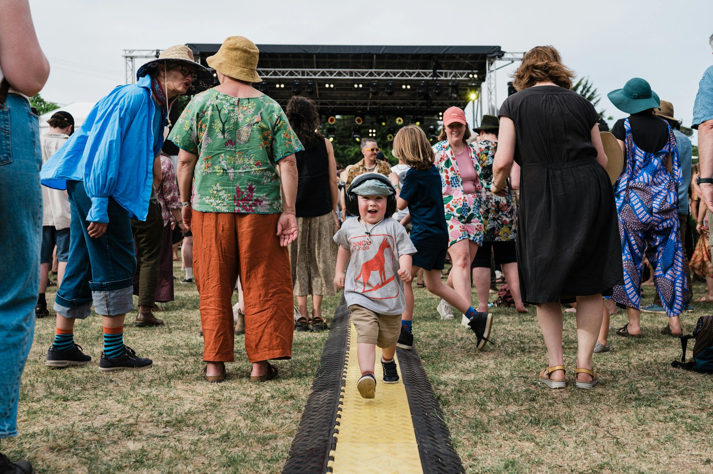 A child runs through the crowd at a festival. There is a stage in the background.