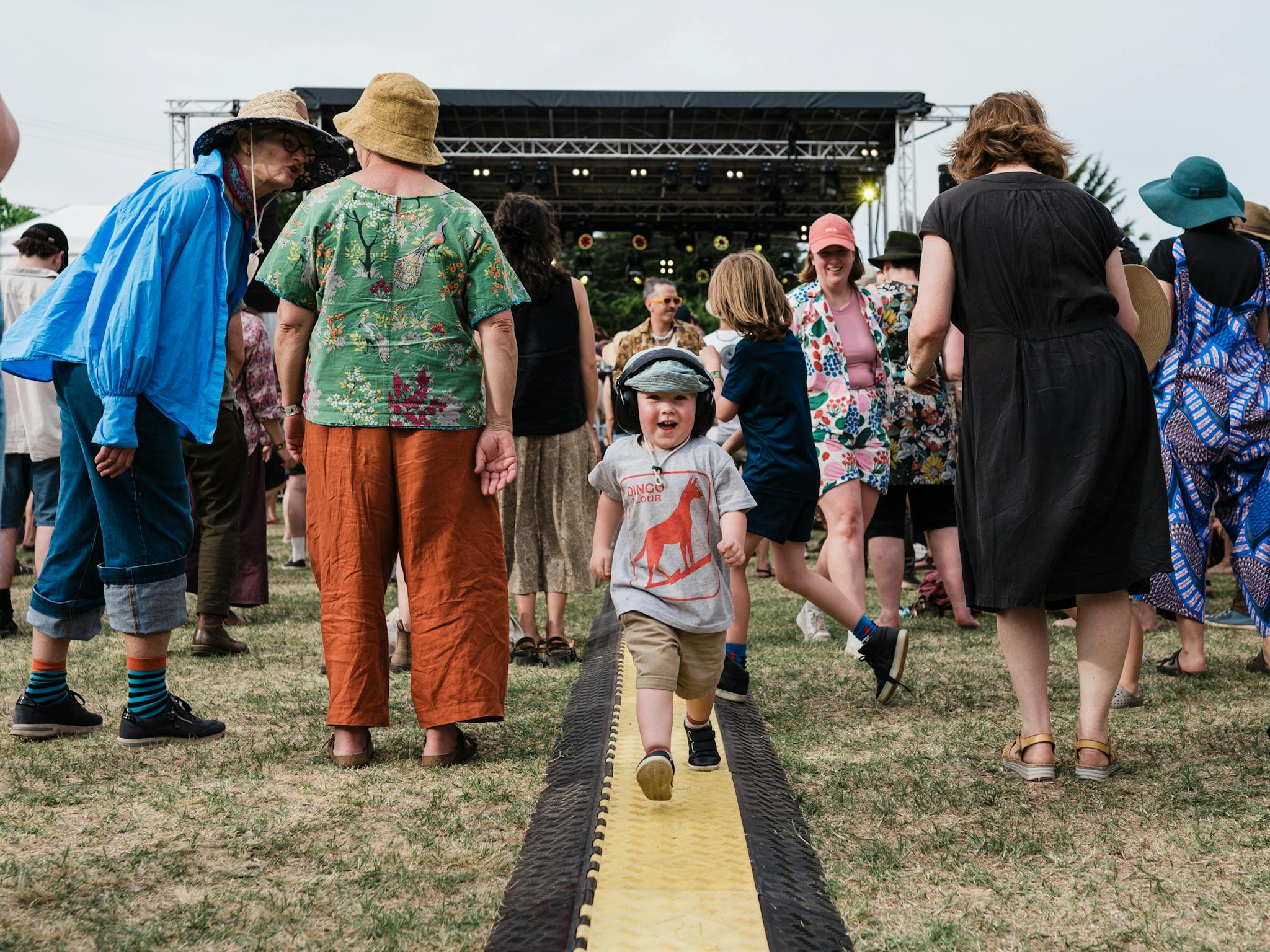 A child runs through the crowd at a festival. There is a stage in the background.