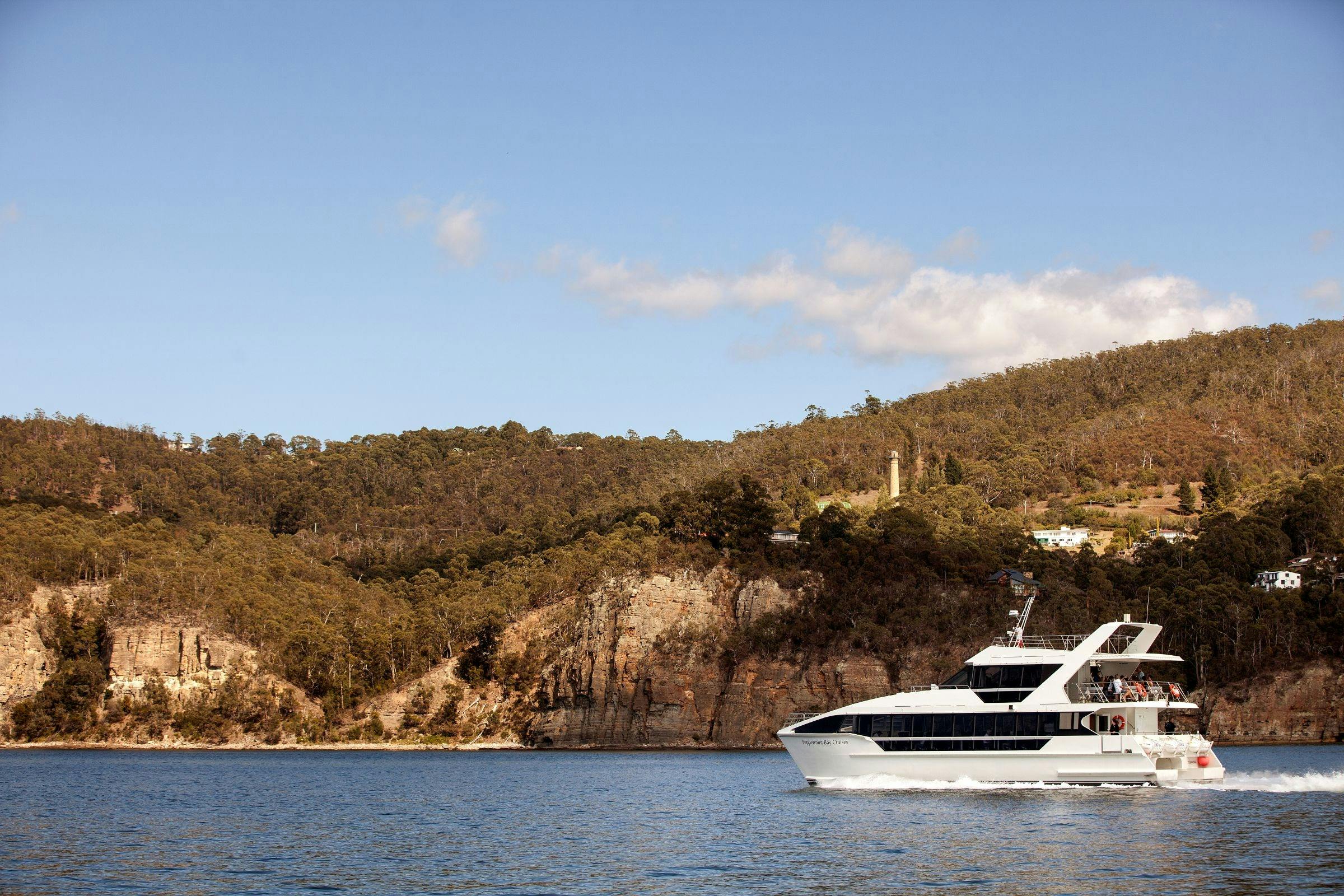 Catamaran cruising past historic shot tower and cliffs