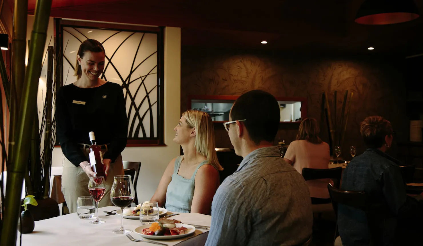 A waitress serving a bottle of wine to a couple dining at The Tamarind restaurant