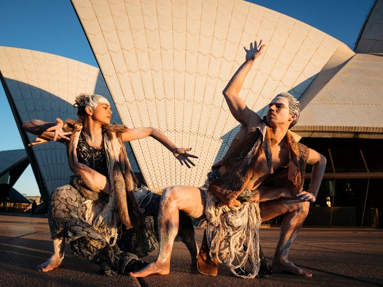 Two dancers hold a pose outside Sydey Opera House. They are in costumes and have paint on them.