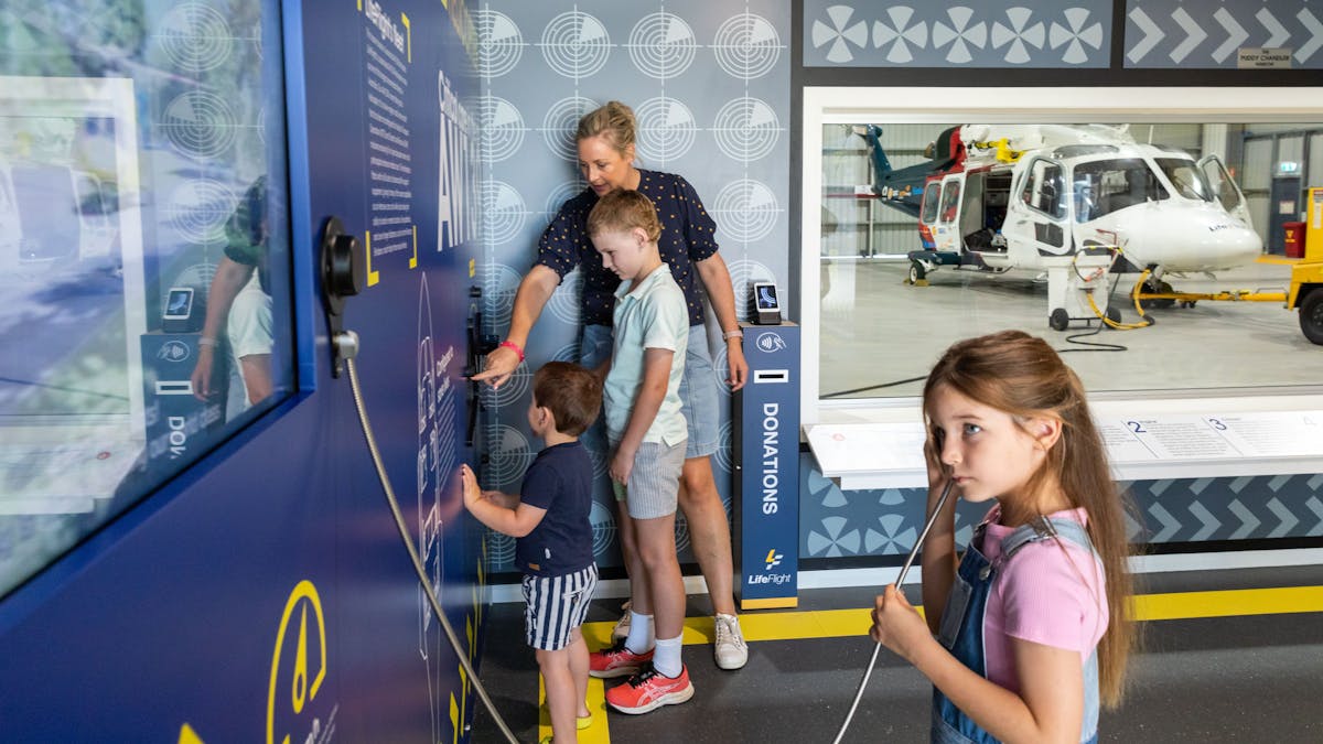 A mother and three children engaging with interactive exhibits with a helicopter in the background