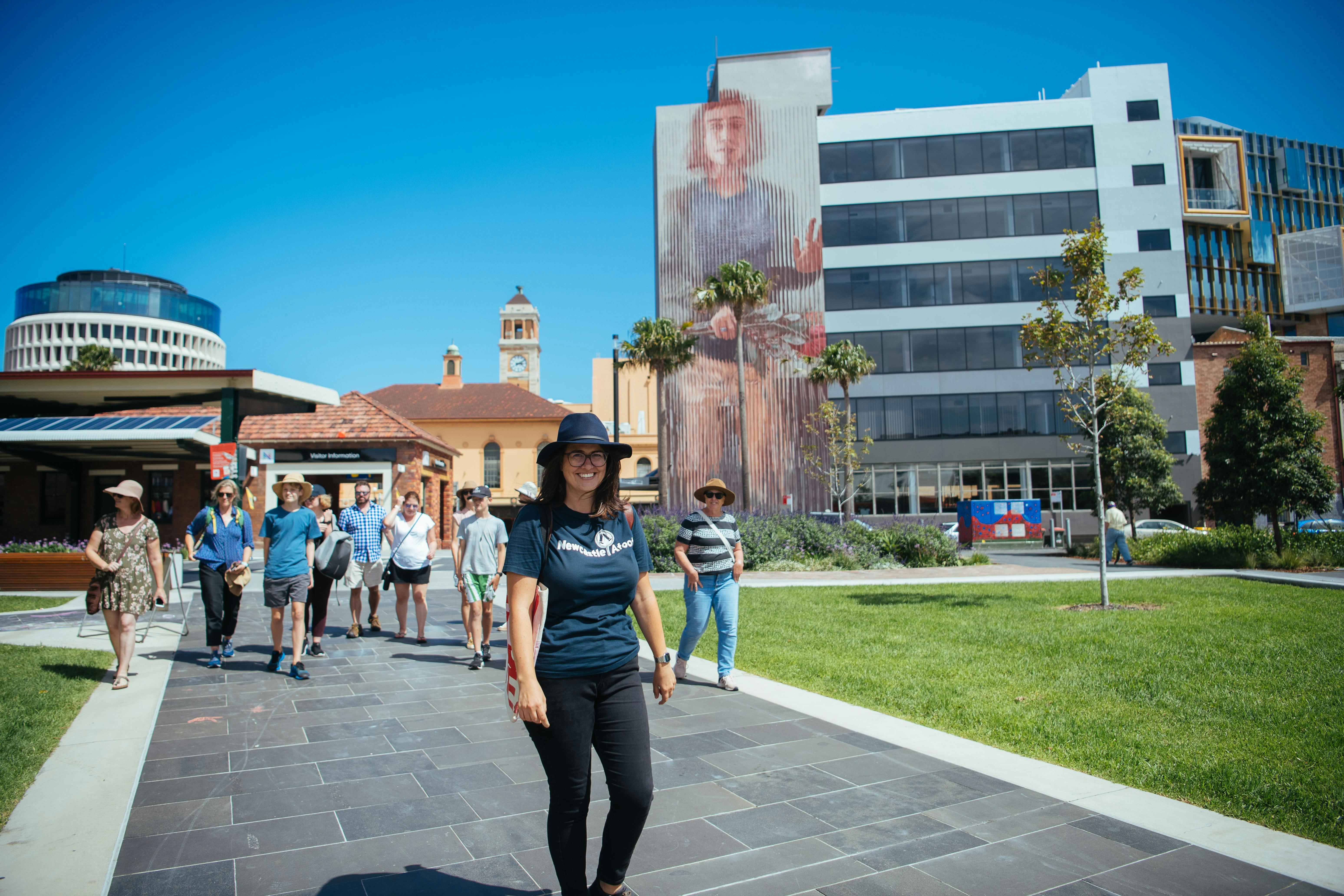 A Newcastle Afoot guide leads a group of guests in front of a large mural of a woman by Fintan Magee