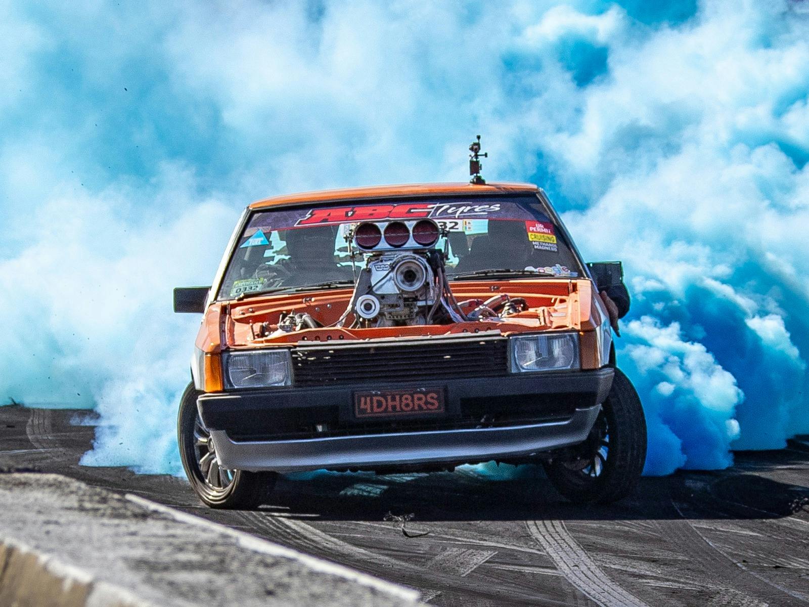 Orange burnout car 4DH8RS driving through a large cloud of tyre smoke on the burnout pad.
